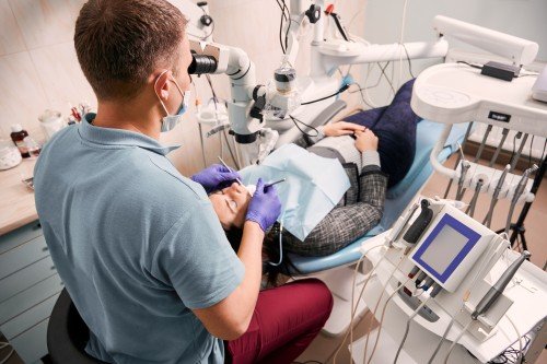 Dentist examining a female patient’s teeth using a dental microscope and specialized instruments in a modern dental clinic