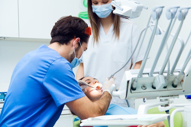 Dental Surgeon performing a dental procedure on a patient with assistance from a dental professional in a modern clinic.