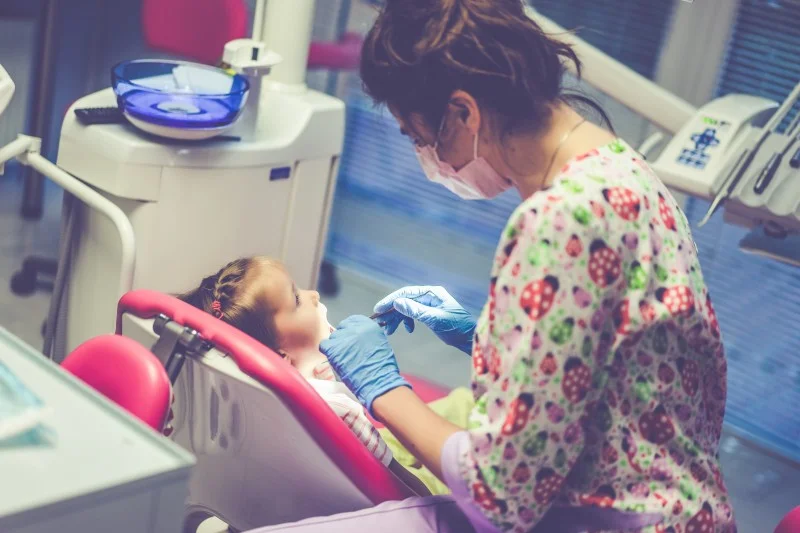 Pediatric dentist examining a young child’s teeth during a dental appointment